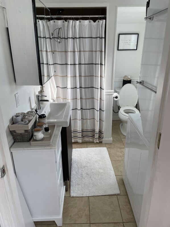 A compact bathroom with a white sink, a toilet, a striped shower curtain, and a small rug.