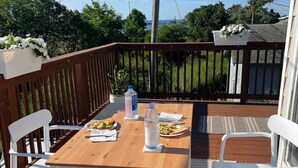 A wooden deck with a table set for two, white chairs, and a potted plant. - Sunset Studio (Branford)