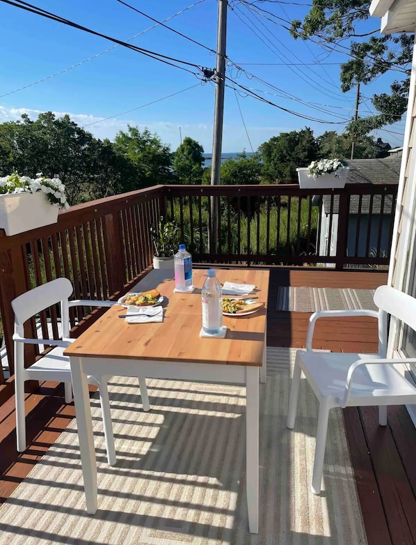 A wooden deck with a table set for two, white chairs, and a potted plant.
