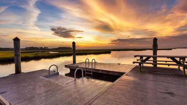 Un molo di legno con una panchina e una piccola piscina, che si affaccia su un bacino d'acqua calma al tramonto.