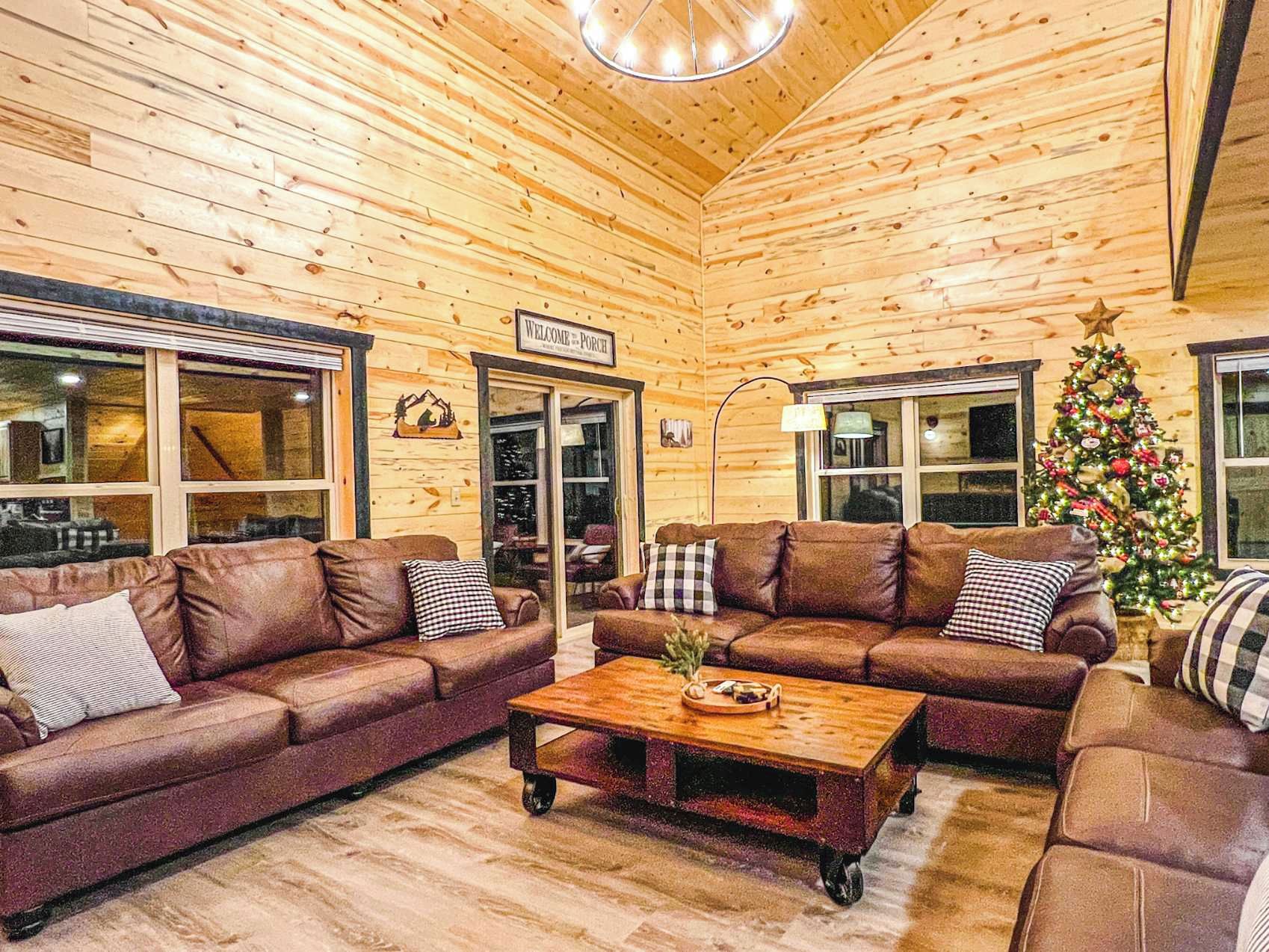 A cozy cabin interior with wooden walls, leather sofas, a coffee table, and a Christmas tree.
