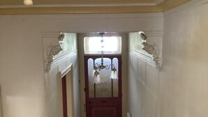 Ein schmaler Flur mit einer roten Tür am Ende, gesäumt von weißen Wänden und einem Deckenventilator.