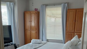 A bedroom with a bed, wooden wardrobe, ceiling fan, and a desk with a lamp.