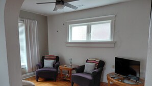 A living room with two armchairs, a wooden coffee table, a television, and a ceiling fan.