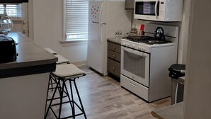 A compact kitchen with a refrigerator, microwave, stove, and a small bar stool.