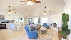 A spacious living area with a sofa, coffee table, and a fireplace. There are ceiling fans, a kitchen area, and a dining space visible. - Beach Front Home in beautiful Playa Encanto gated community 3bed/3bath (Playa Encanto)