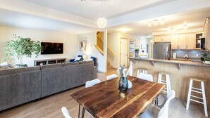 Una sala de estar moderna con una mesa de comedor de madera, un sofá gris y un televisor en la pared.