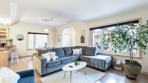 Una sala de estar moderna con un sofá seccional gris, una mesa de centro blanca y un ventanal con vistas al exterior.
