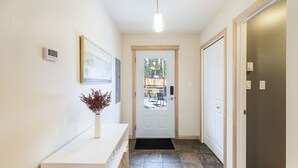 A hallway with a white console table, a vase with dried plants, a framed picture, and a door leading to an outdoor area with chairs and a table. - Mountain Haus w/ HOT TUB & large backyard w/firepit. Only 7 mins to downtown (Whitehorse)