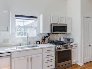 Cucina con mobili bianchi, piano cottura in acciaio inossidabile, forno a microonde e finestra vista casa.