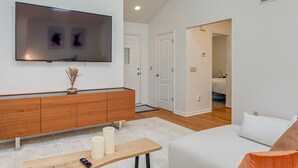 A modern living room with a flat-screen TV, wooden console, white sofa, and a small table with candles.