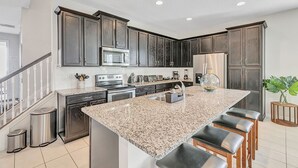A modern kitchen with dark wood cabinets, stainless steel appliances, and a granite island with bar stools.