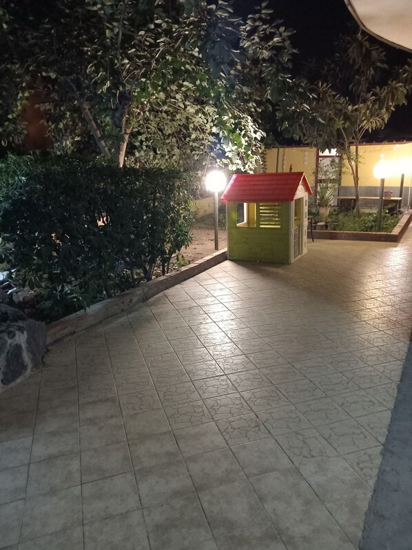 Een klein, groen kioskje met een rood dak, omgeven door groen en een betegeld pad.