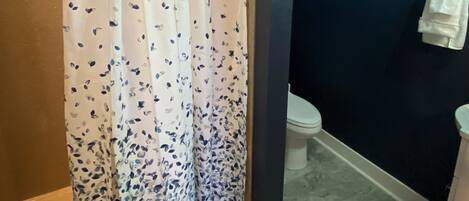 Un baño con cortina de ducha, inodoro y toallero.