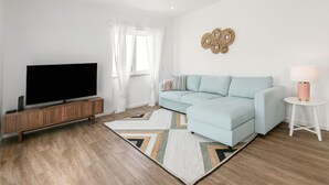 A modern living room with a sectional sofa, a flat-screen TV on a wooden console, a patterned rug, and a decorative wall piece.