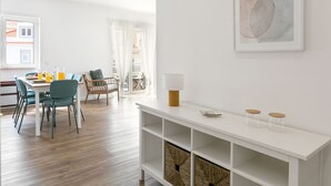 A modern dining area with a white table, teal chairs, and a white console table with a lamp and two glass jars.