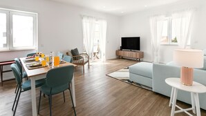 A modern living room with a dining area, a sofa, a TV, and a lamp.