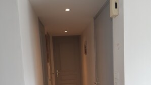 En smal hall med trägolv, vita väggar och en stängd dörr längst in.