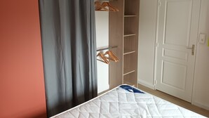 Ett sovrum med en säng, grå gardiner, en trägarderob och en vit dörr.