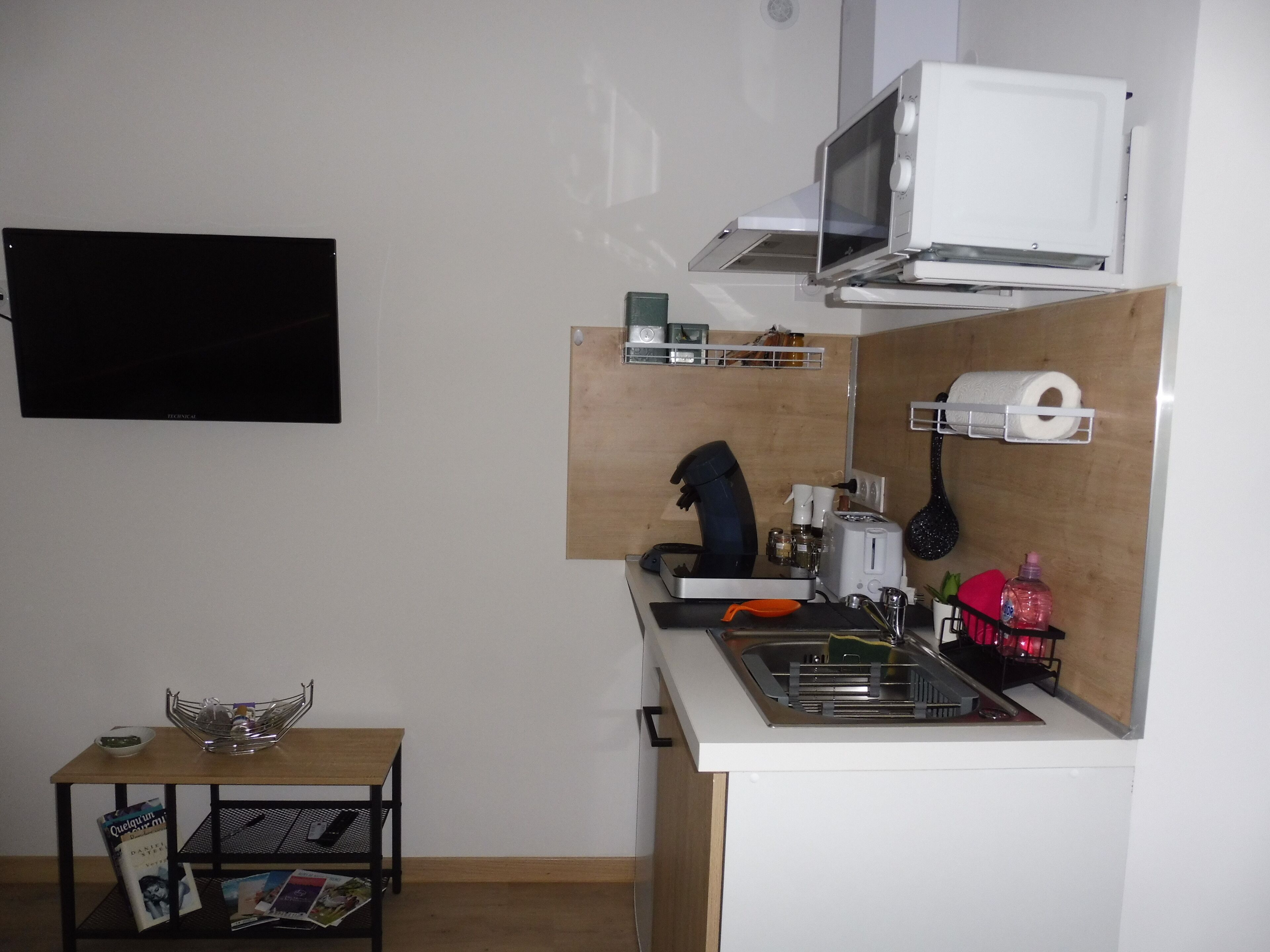 Eine kleine Küchenzeile mit Mikrowelle, Toaster, Spüle und einem Tisch mit Schüssel und Zeitschriften.