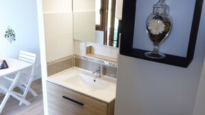Un baño con un lavabo blanco, un espejo y un jarrón enmarcado en la pared.
