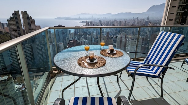 A balcony with a glass table and chairs, overlooking a cityscape with mountains in the distance. - TORRE LUGANO sea view apartment (Benidorm)