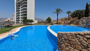 A swimming pool with a stone wall and a tall building in the background. - TORRE LUGANO sea view apartment (Benidorm)