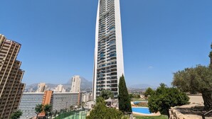 A tall, modern high-rise building with multiple balconies, surrounded by other buildings and a clear blue sky. - TORRE LUGANO sea view apartment (Benidorm)
