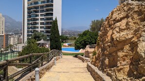 A view of a swimming pool area with a stone wall and a staircase leading down to the pool. - TORRE LUGANO sea view apartment (Benidorm)