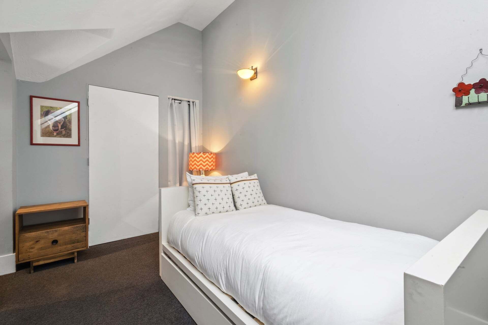A bedroom with a single bed, a nightstand, a lamp, a framed picture, and a wall-mounted light fixture.