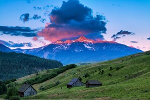 A mountainous landscape with two wooden cabins on a grassy hill.