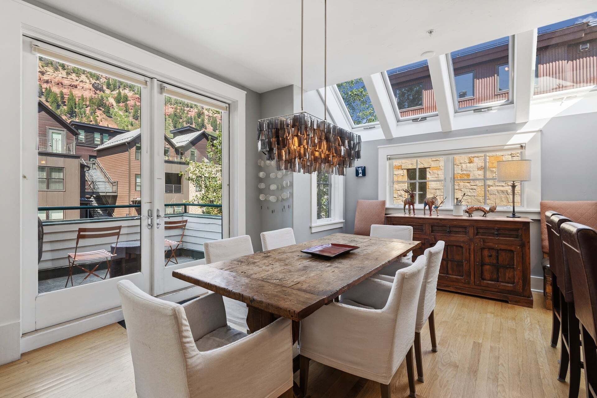 A modern kitchen with a large dining table, white chairs, and a view of a mountainous landscape through large windows.