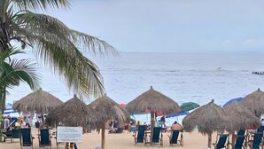 A beach with thatched umbrellas and lounge chairs, a sign indicating a restaurant, and palm trees. - Condominium Playa Bonita (Puerto Vallarta)
