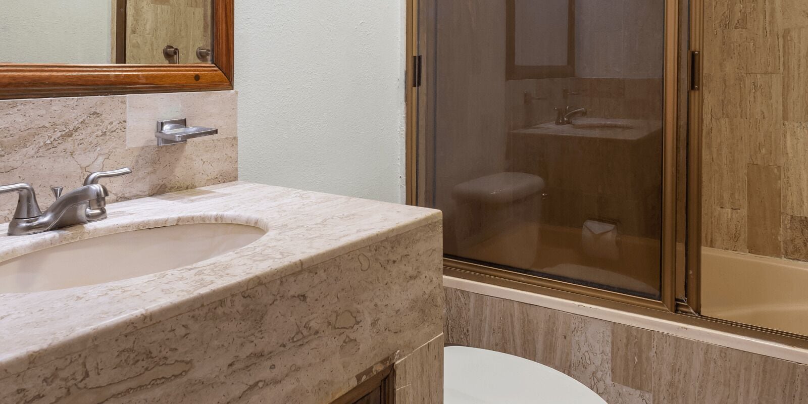 A bathroom with a marble sink, a toilet, and a glass-enclosed shower.