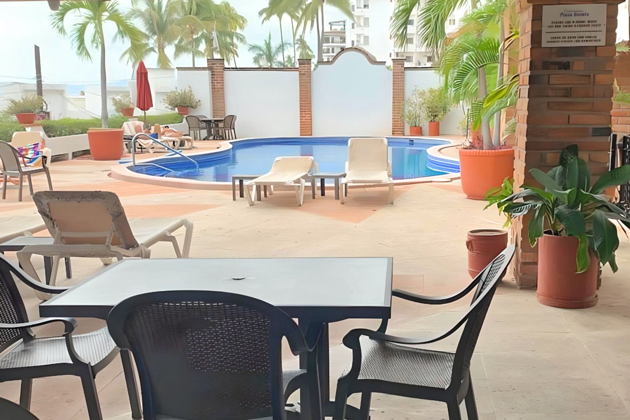 Zona de piscina en la azotea con sillones de descanso, una mesa y plantas en macetas.
