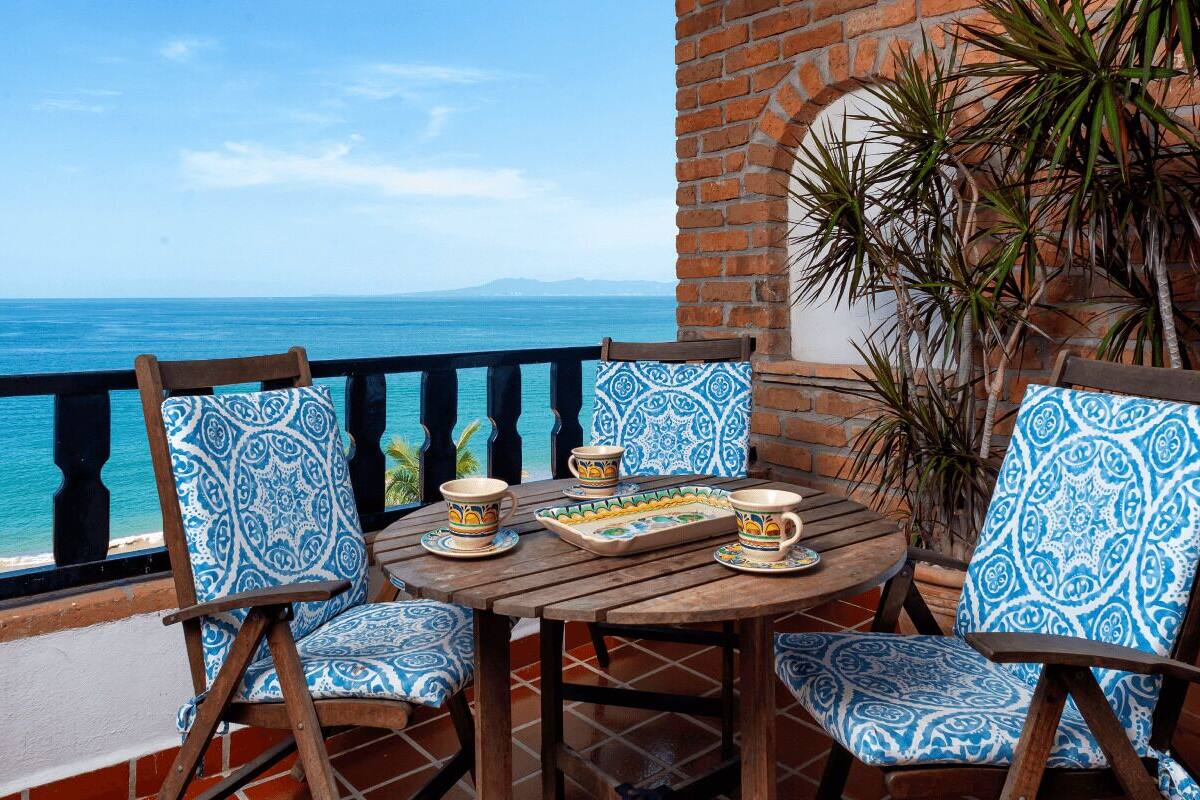 Una terraza con vistas al mar, con una mesa de madera, sillas y un muro de azulejos.