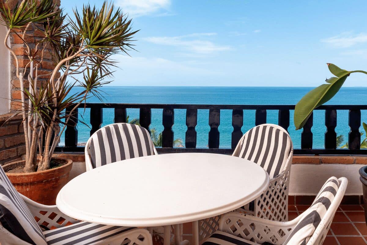 Un balcón con una mesa redonda y sillas a rayas, con vistas a la costa.