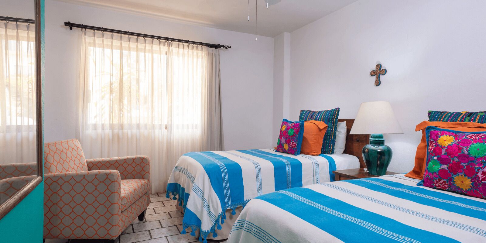 Habitación de hotel con dos camas, una silla, una lámpara y una cruz en la pared.