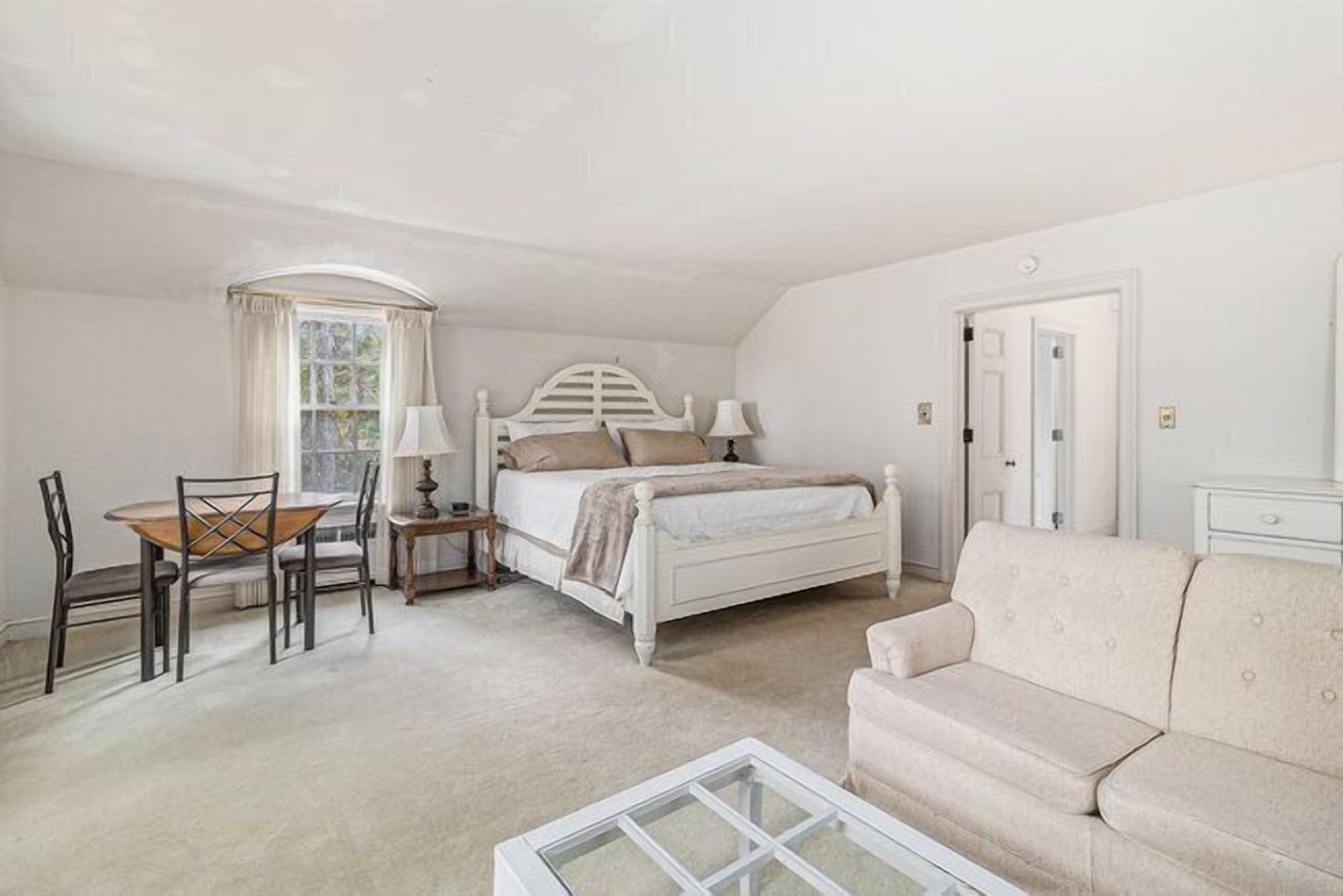 A bedroom with a bed, a chair, a table, and a sofa.