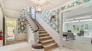Eine prächtige Treppe mit einer Chandelieber, ein Wohnzimmer mit Sofa und Sesseln sowie ein Blick ins Freie.