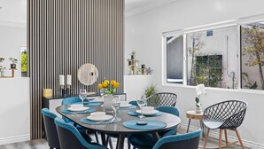 A modern dining area with a round table, blue upholstered chairs, and a vertical striped partition. - Stylist Home In Convenient  Location New Listing Special Book Now! (Temple City)