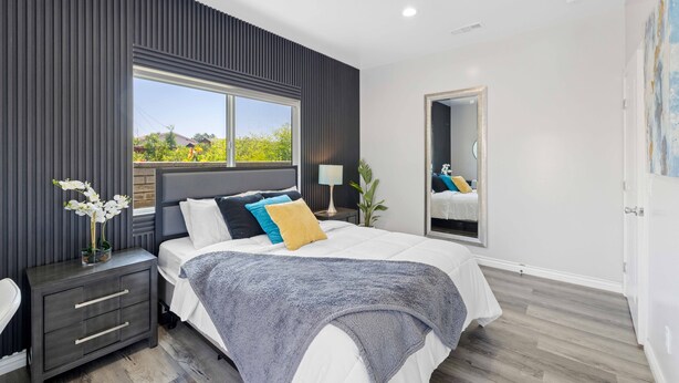 A modern bedroom with a large bed, a nightstand, a window, and a mirror. - Stylist Home In Convenient  Location New Listing Special Book Now! (Temple City)