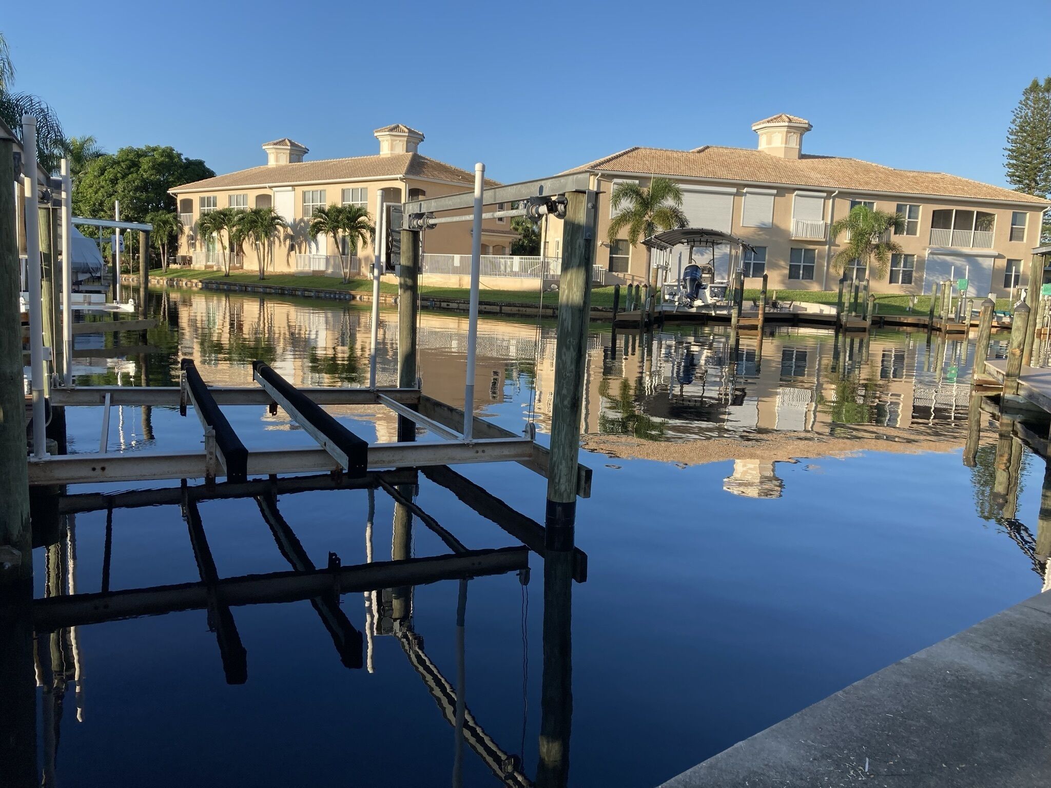 Uma marina com barcos atracados, superfície de água calma refletindo os edifícios e um céu limpo.