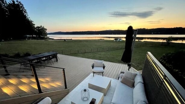 A deck with a sofa and table, overlooking a body of water and grassy area. - Hood Canal Beach Retreat (Belfair)