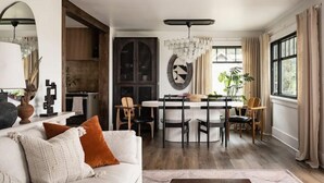 A modern living room with a white sofa, a dining table with chairs, and a large window with curtains. - Hood Canal Beach Retreat (Belfair)