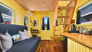 A compact, yellow-themed cabin with a bed, a small table, and a kitchen area. - The Arthur - Custom Tiny Home w/ Train Vibe (Portland)