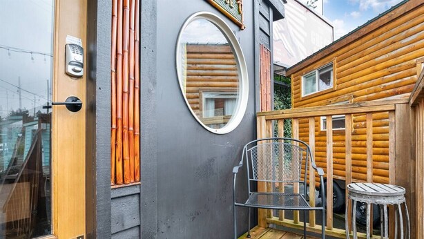 A wooden deck with a metal chair and stool, a circular mirror, and a door with a keyhole. - The Bamboo - Custom Tiny Home w/ Bamboo Vibe (Portland)