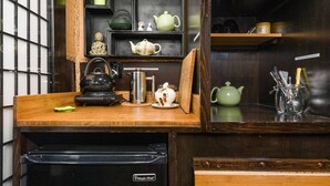 A kitchen with a wooden countertop, a kettle, a teapot, and a coffee maker. There is a shelf with various kitchen items and a small Buddha statue. - The Bamboo - Custom Tiny Home w/ Bamboo Vibe (Portland)