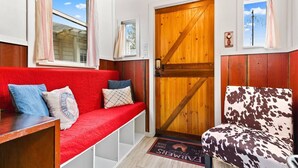 Un interior acogedor con un sofá rojo, un sillón estampado con vacas y una puerta de madera.