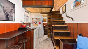 Una cocina con detalles de madera, un hervidor rojo y una escalera que sube a otro nivel.